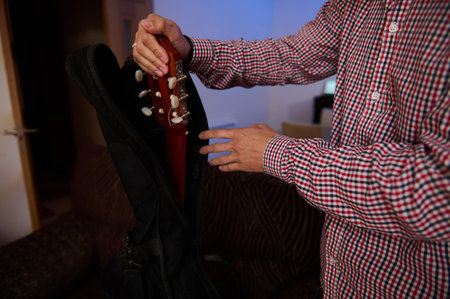A person carefully places a guitar into its carrying case indoors. The environment appears comfortable and relaxed, ideal for music enthusiasts preparing for travel or storage.の写真素材