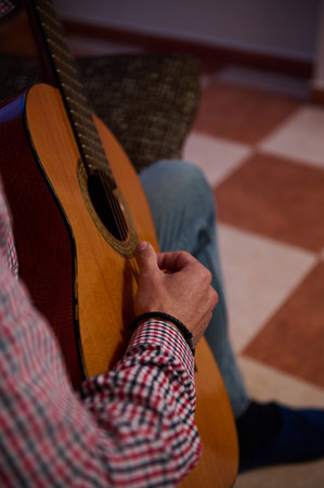 A person is strumming the strings of an acoustic guitar indoors on a tiled floor. Capturing the...