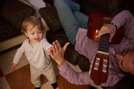 An adorable child interacts with their parent as they play a guitar, showcasing a warm and joyful family bond in a comfortable, inviting home setting.の写真素材
