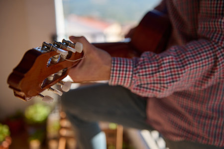 Close-up image of a person playing a classical guitar on a sunny balcony, highlighting the...