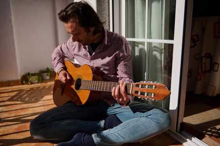 Someone playing a classical acoustic guitar while enjoying sunlight on a home patio.