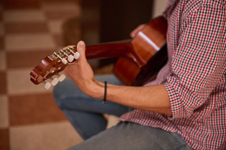 A close-up view of a person strumming an acoustic guitar in an indoor setting, wearing casual clothing. The scene highlights the guitar's features and the individual's relaxed posture.の写真素材