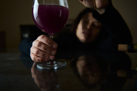 A contemplative individual holding a glass of deep red wine, emphasizing introspection and the rich texture of the beverage.の写真素材