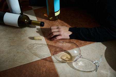 A view of wine bottles, a spilled wine glass, and a hand on a tiled floor.の写真素材