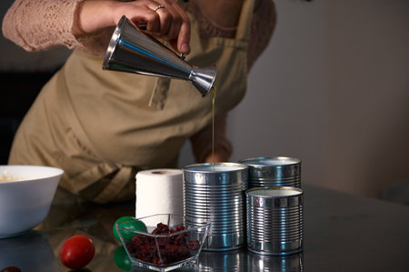A woman in an apron pours oil into metal cans while preparing food in the kitchen, showcasing...