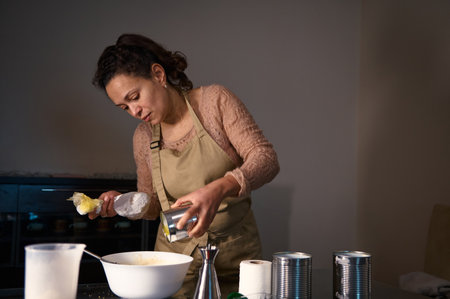 A woman wearing an apron carefully prepares ingredients in a kitchen for a recipe.