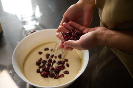 Baker preparing a delicious batter by adding dried fruits. Focus on hands and ingredients, giving a...