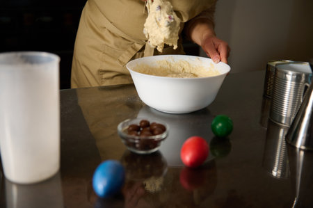 A person in an apron prepares dough in a bowl on a surface with colored eggs symbolizing Easter. The scene reflects holiday celebrations and homemade baking activities.の写真素材