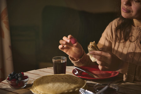 A person enjoying a cozy breakfast, featuring crepes, fresh berries, and a warm drink. Ideal for concepts around relaxation, comfort food, cozy mornings, and indulgent dining traditions.の写真素材