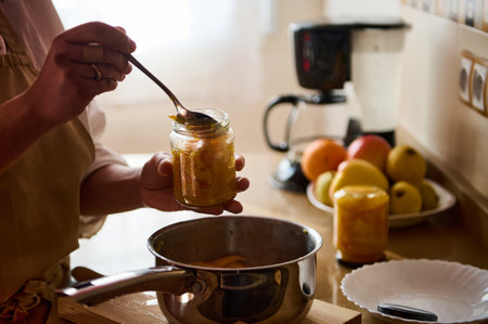A close-up of a jar being filled with homemade preserves in a cozy kitchen setting. Various fresh fruits and kitchen utensils are seen in the background, creating a warm and inviting atmosphere.の写真素材