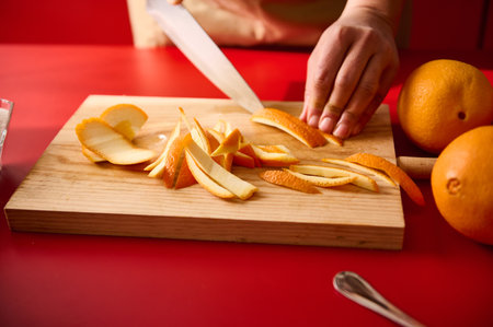 Close-up of a hand preparing orange peels on a wooden board with a knife.の写真素材