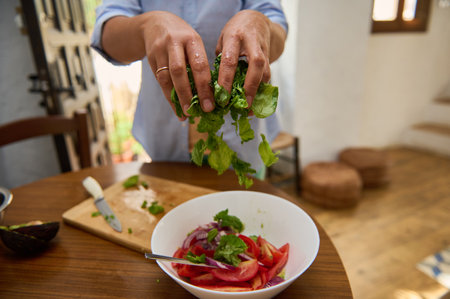 Delicious salad preparation involving fresh vegetables including lettuce and tomatoes in a homely kitchen.の写真素材