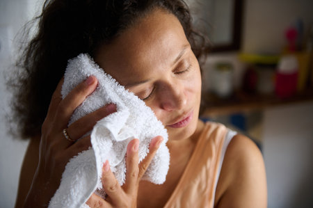 A woman softly pressing a clean white towel to her face, showcasing skincare and self-care in a home environment. The image highlights relaxation, hygiene rituals, and a calm lifestyle in a skincare context.の写真素材