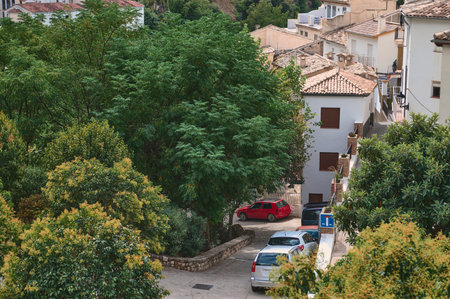 Serene village scenery showcasing Mediterranean houses surrounded by lush green foliage and parked cars on quaint streets, embodying the tranquility and charm of traditional European architecture in a countryside setting.の写真素材