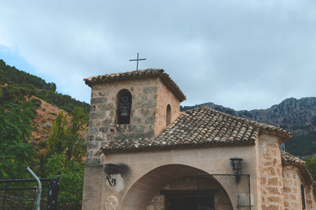 A rustic stone church with a bell tower, nestled in a scenic mountainous area with vibrant natural surroundings and a partly cloudy sky, showcasing historical and architectural beauty.の写真素材
