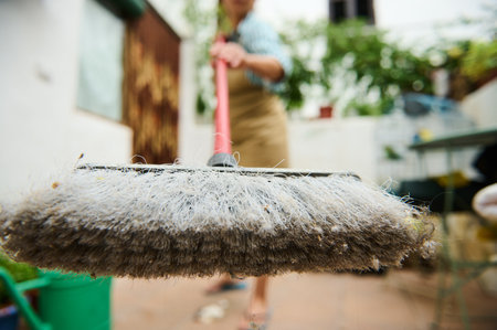 Dirt-laden broom being used to clean an outdoor area with greenery in the background.の写真素材