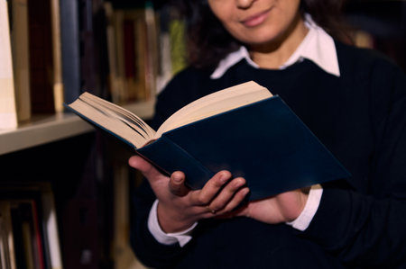 A person holding and reading a book while standing near shelves in a library, showcasing a quiet and studious atmosphere, perfect for learning, research, or personal development.の写真素材