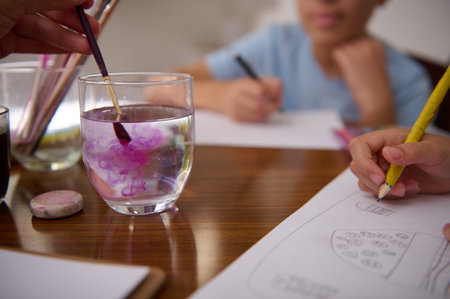 Children participating in an art session, drawing on paper and mixing paint in water.
