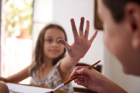 A child engaging in an artistic painting activity, joyfully displaying a hand covered in paint. Encouraging creativity and artistic exploration in a home environment with children enjoying creative pursuits.の写真素材