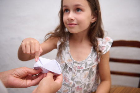 A young girl interacts with a paper origami creation, displaying interest and creativity. The scene conveys learning, teamwork, and the imaginative nature of crafting activities among children and adults.の写真素材