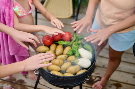 A family gathered around an outdoor barbecue grill cooking a variety of fresh vegetables, including potatoes and peppers, while enjoying the warm atmosphere and shared moments. A symbol of outdoor cooking and bonding.の写真素材
