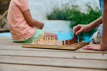 Two kids enjoy a strategic chess game on a sunny day, fostering concentration and fun. Their creativity and focus reflect joyful moments in a peaceful outdoor setting, emphasizing community and engagement.の写真素材