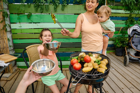 A lively family barbecue in a vibrant backyard featuring a joyful moment and fresh grilled vegetables.の写真素材