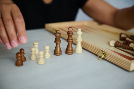 A close-up view of a person organizing wooden chess pieces on a smooth light-colored surface,...