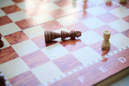 A wooden chess king lies toppled on a board indicating a game's conclusion or victory. The emotional scene focuses on strategy, competition, and the symbolic representation of challenges and victories in chess.の写真素材