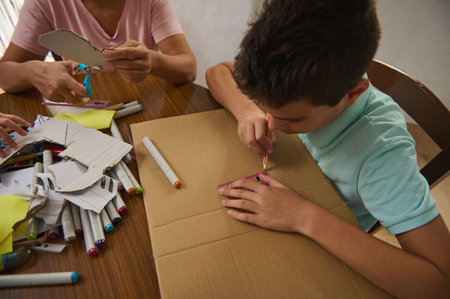 A young boy actively engages in a creative cardboard crafting project with adult guidance.の写真素材