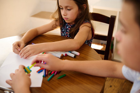 Young children sitting at a table focusing on coloring and crafting, showcasing childhood...
