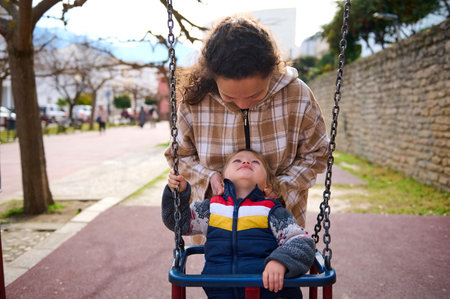 A mother lovingly interacts with her child as they enjoy time outdoors at a park playground, emphasizing the bond and joyful connection between parents and children.の写真素材