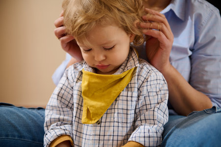 A loving mother adjusts her little son's outfit. The child sits peacefully, conveying warmth and affection. A tender moment reflecting love and family care.の写真素材