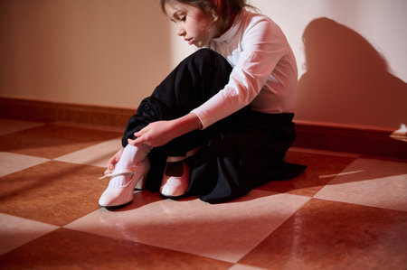 A young girl in elegant attire focuses on fastening her white shoes. The warm sunlight creates a relaxing atmosphere.の写真素材