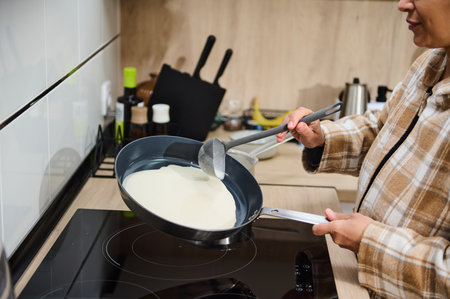 A woman prepares crepe batter on an induction stove in a modern kitchen. The scene conveys home cooking, culinary enjoyment, and a relaxed kitchen atmosphere. Ideal for food and domestic themes.の写真素材