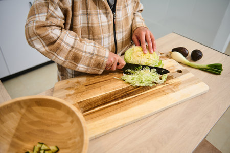 A young woman wearing a plaid shirt cuts fresh vegetables, preparing salad in a cozy kitchen. The scene emphasizes healthy eating and domestic lifestyle, featuring fresh, natural ingredients.の写真素材
