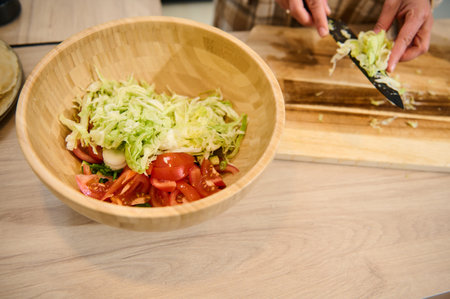 A home-cooked fresh salad being prepared in a cozy kitchen. Vibrant vegetables are chopped and placed in a wooden bowl, emphasizing healthy eating and culinary creativity.の写真素材