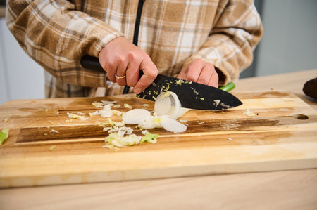 A person wearing casual clothes slices an onion on a wooden cutting board in a kitchen setting. This image symbolizes cooking, preparation, and healthy eating activities in a home environment.の写真素材