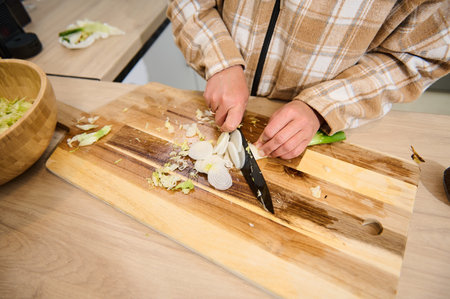 A person cuts fresh vegetables on a wooden cutting board in a bright kitchen. This image conveys healthy food preparation, cooking routines, and the essence of homemade meals.の写真素材