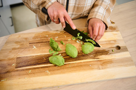 A person carefully slicing avocado and green onions on a wooden cutting board in a kitchen setting....