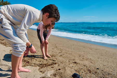 Children explore the sandy beach barefoot on a sunny day, enjoying the ocean waves nearby, illustrating family bonds and relaxation by the seashore.の写真素材