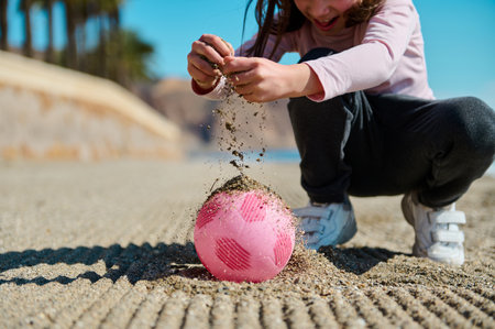 A happy child enjoys playing with a pink ball on a sunny sand beach, surrounded by nature.の写真素材