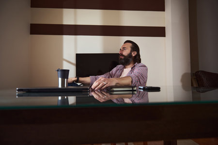 Professional setting with a man reflecting at an office desk. Home workspace for freelance or remote...