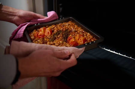Home-cooked dish featuring baked beans with cherry tomatoes and rosemary, freshly taken out of the oven, capturing the warmth of homemade meals.の写真素材