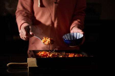 A person serves freshly cooked baked beans garnished with herbs into a blue bowl, captured in a...