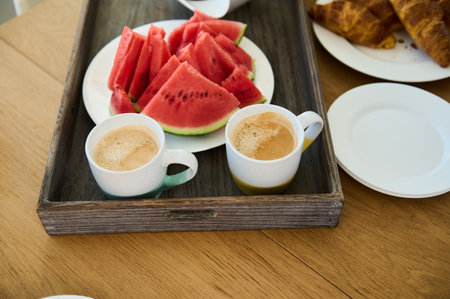 A delightful breakfast featuring freshly brewed coffee, watermelon slices, and golden croissants served in a cozy setting.の写真素材
