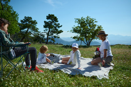 Group of family members spending quality time together having a picnic in a scenic natural mountain setting with a bright sunny sky.の写真素材