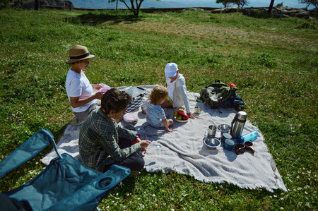 A family enjoys a refreshing picnic in the mountain wilderness. Surrounded by nature, they share moments of happiness and connection under the sun.の写真素材
