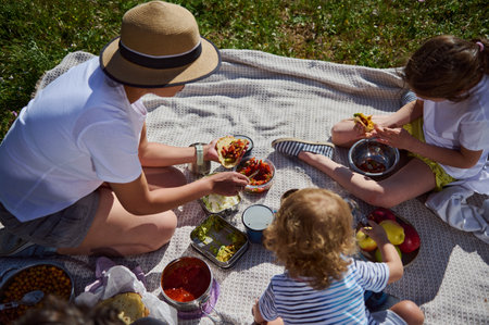 A joyful outdoor picnic scene with a mother and her children enjoying tacos in a natural, sunny setting. Highlights happiness, family time, and healthy outdoor activities.の写真素材