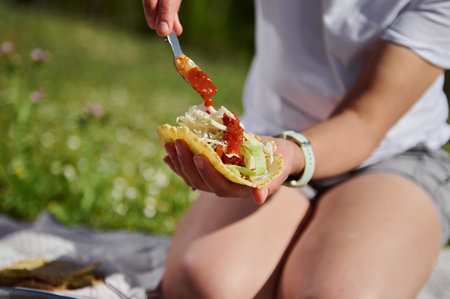A person crafts a taco amidst a vivid summer picnic, showcasing fresh ingredients and outdoor joy under the warm sunlight.の写真素材